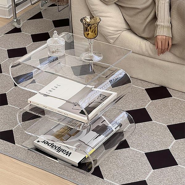 a glass coffee table with magazines on it in front of a couch and checkered floor