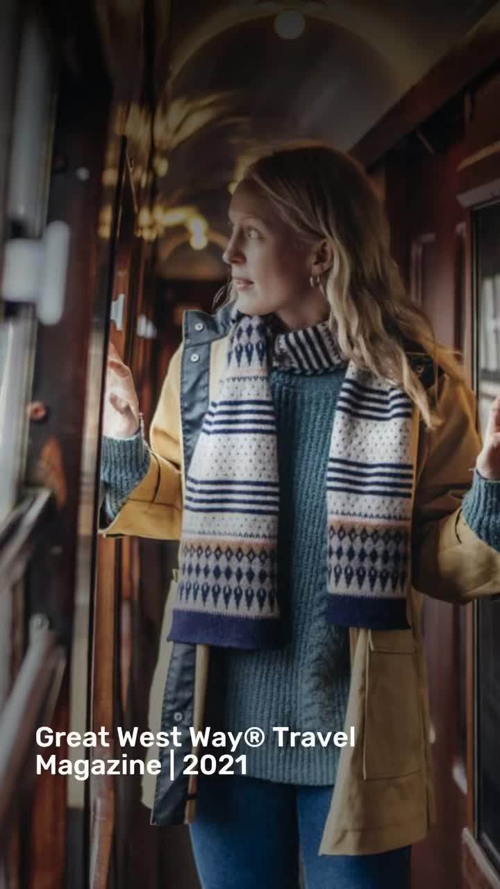 a woman standing in front of a window wearing a sweater and scarf with the words great west way travel magazine on it