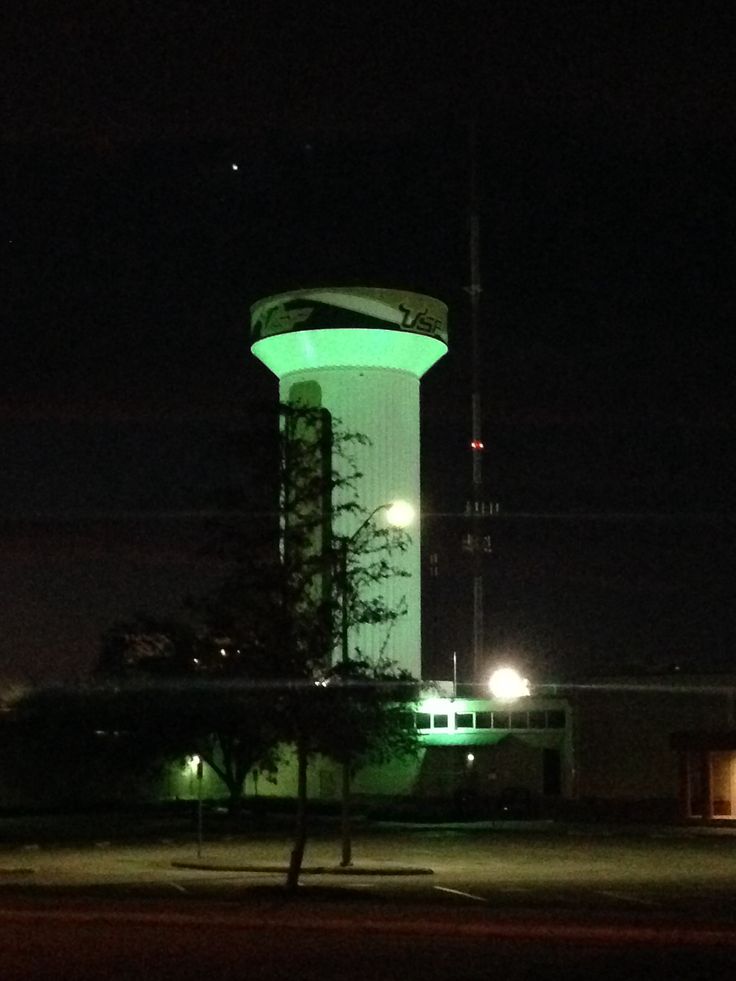 a large tower lit up at night with green lights on it's sides and trees in the foreground