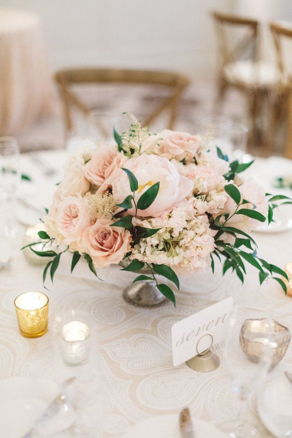 a centerpiece with flowers and greenery sits on a table at a wedding reception