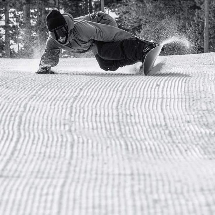 a man riding a snowboard down the side of a snow covered slope with trees in the background