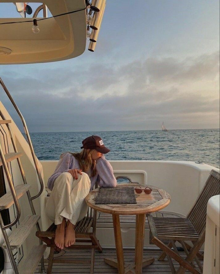 a woman sitting at a table on top of a boat next to the ocean and looking out over the water