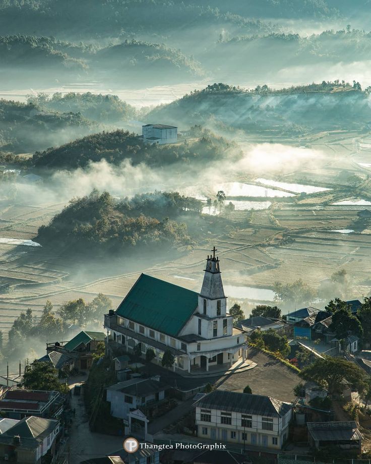 an aerial view of a church surrounded by fog and low lying hills in the distance