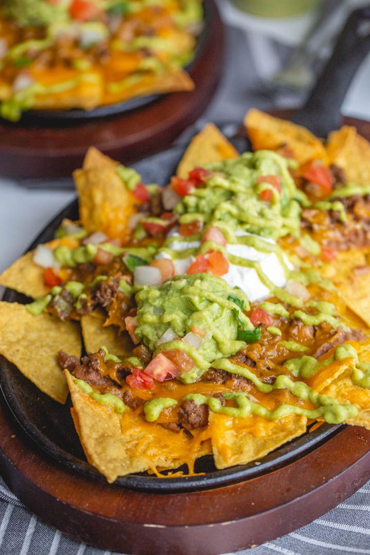 nachos with meat, cheese and guacamole on a wooden platter