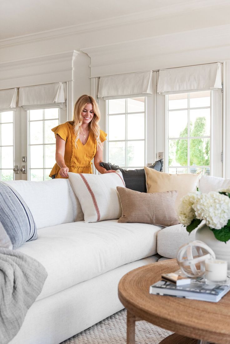 a woman sitting on top of a white couch in a living room next to windows
