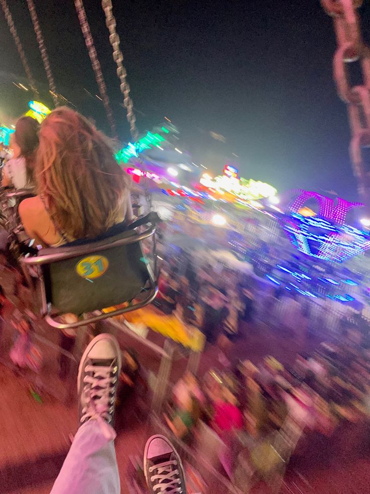 a person sitting on a swing at an amusement park with their feet in the air
