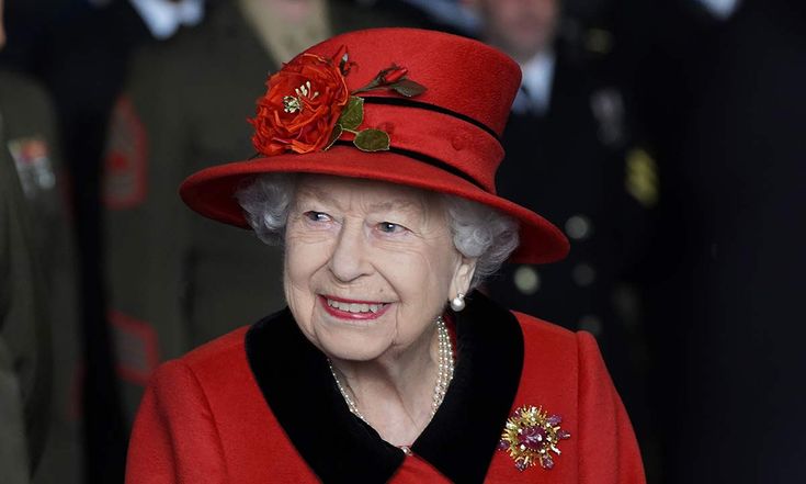 an older woman wearing a red coat and hat with flowers on her head, in front of other people