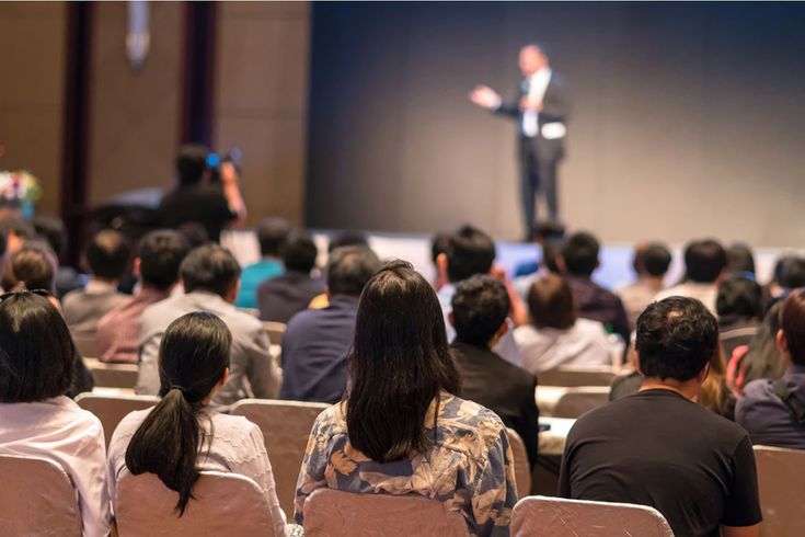 a man standing in front of a crowd of people at a conference or meeting hall