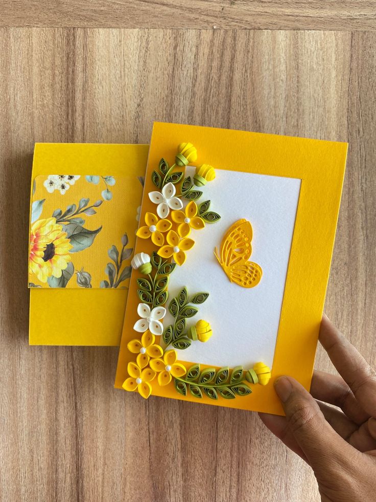 someone is holding two cards with flowers on them, one yellow and the other white