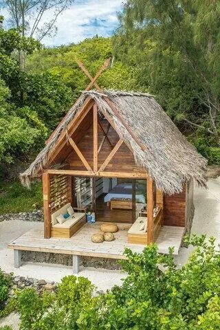 a small wooden cabin with a thatched roof in the middle of trees and sand
