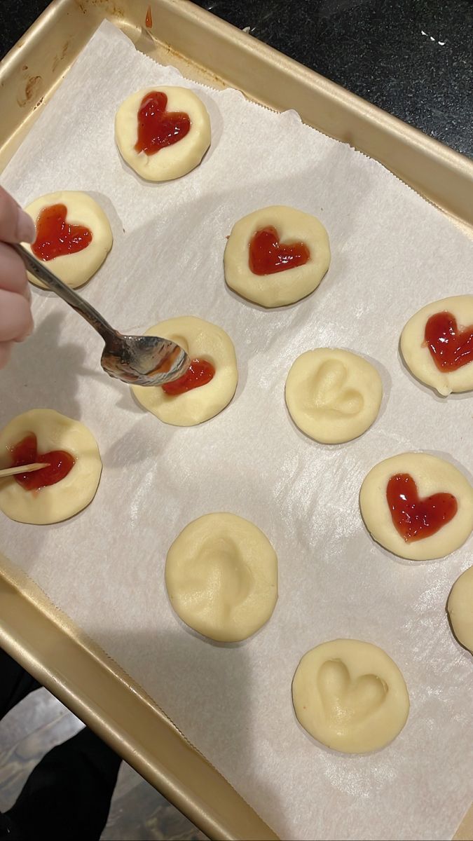someone is spreading ketchup on heart shaped pastries in the baking pan with a spoon