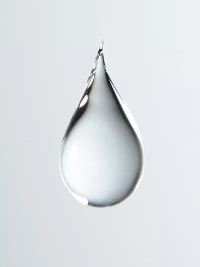 a drop of water that is floating in the air on a white surface with no one around it
