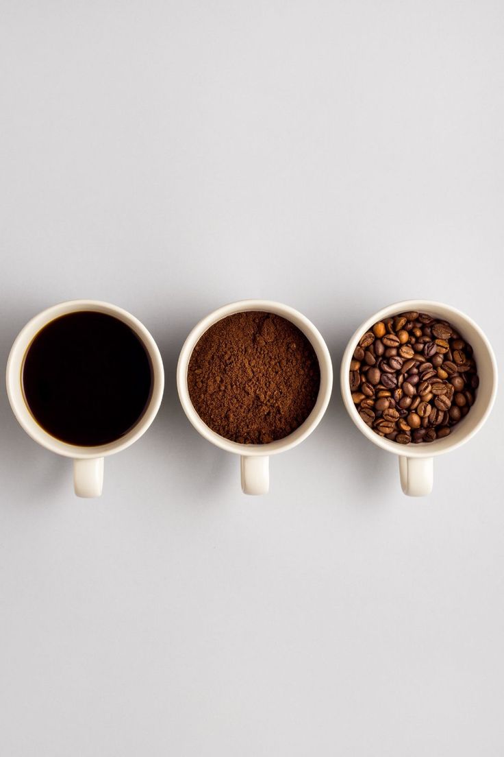 three coffee mugs filled with different types of coffee beans and ground coffee next to each other