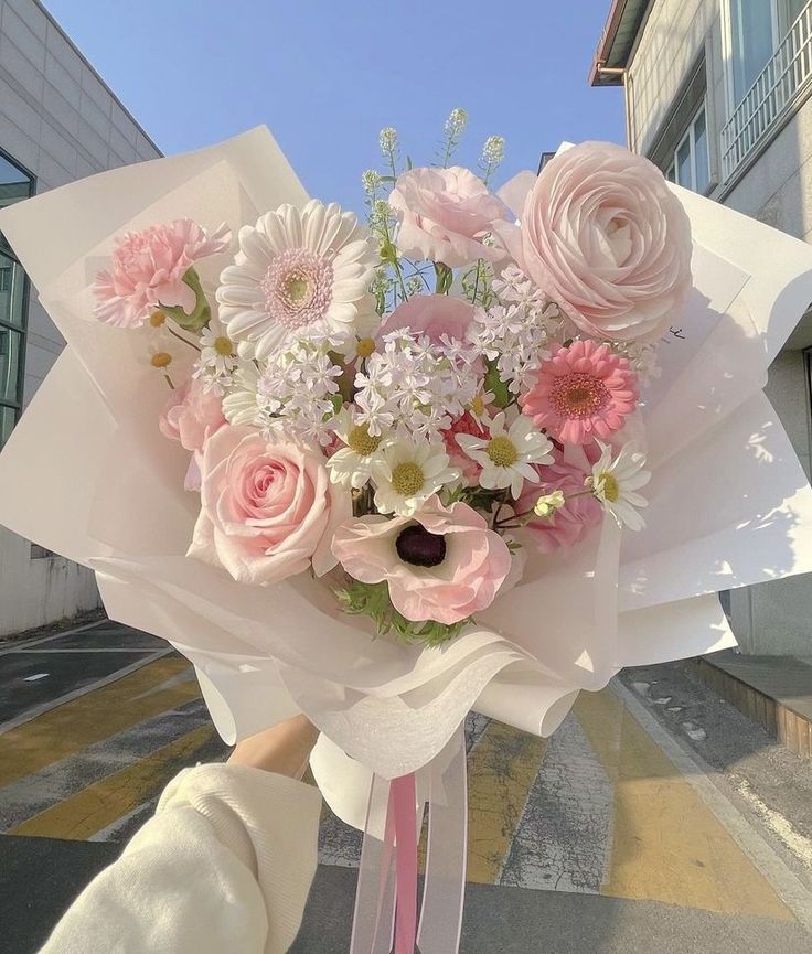 a bouquet of pink and white flowers is held by a woman's hand in front of a building