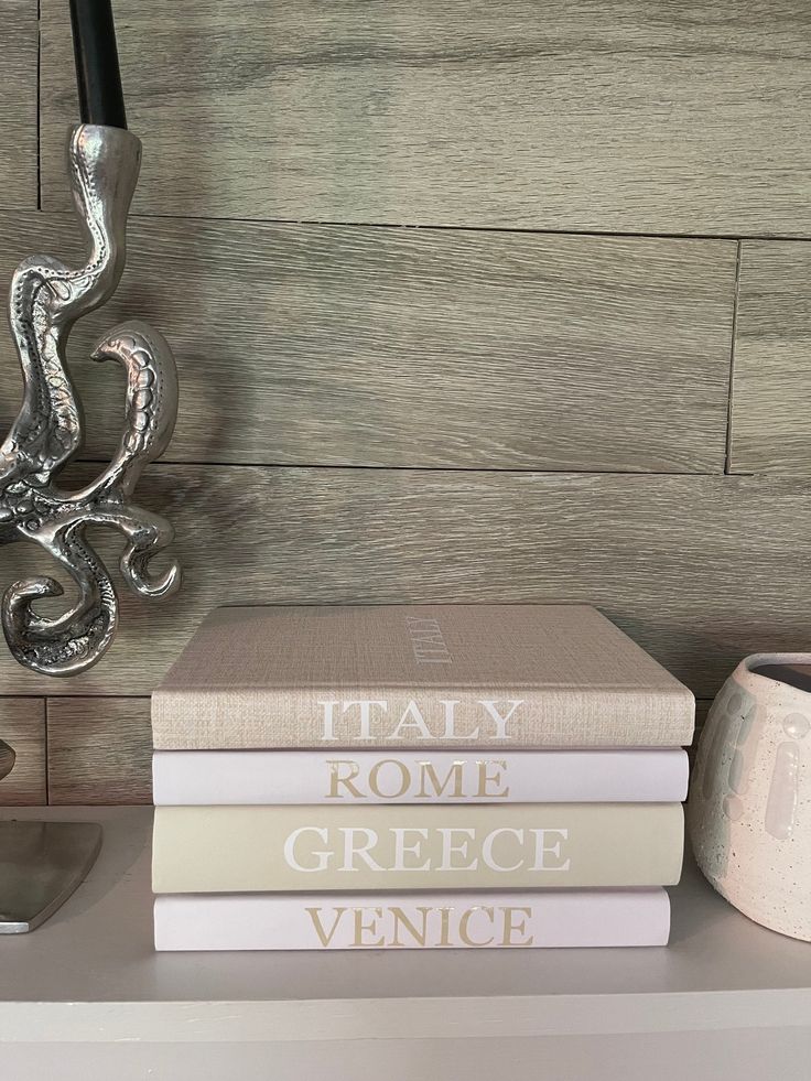 three books sitting on top of a white shelf next to a vase and candle holder