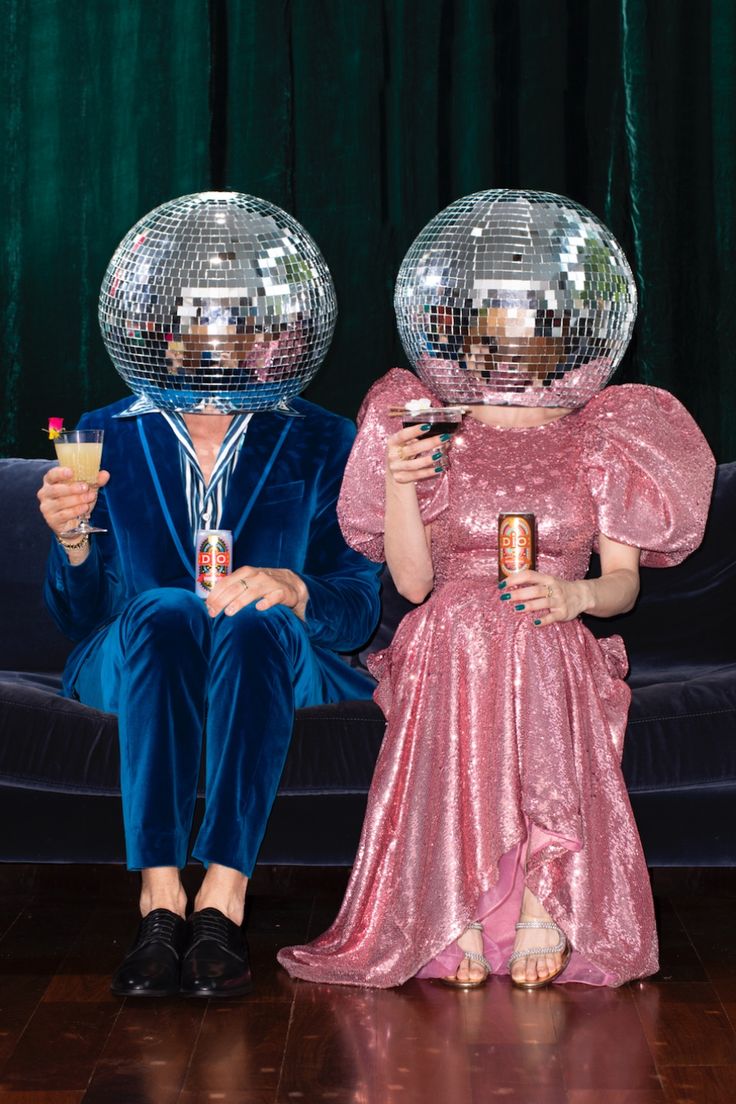 two people sitting on a couch with disco balls over their heads and one holding a drink