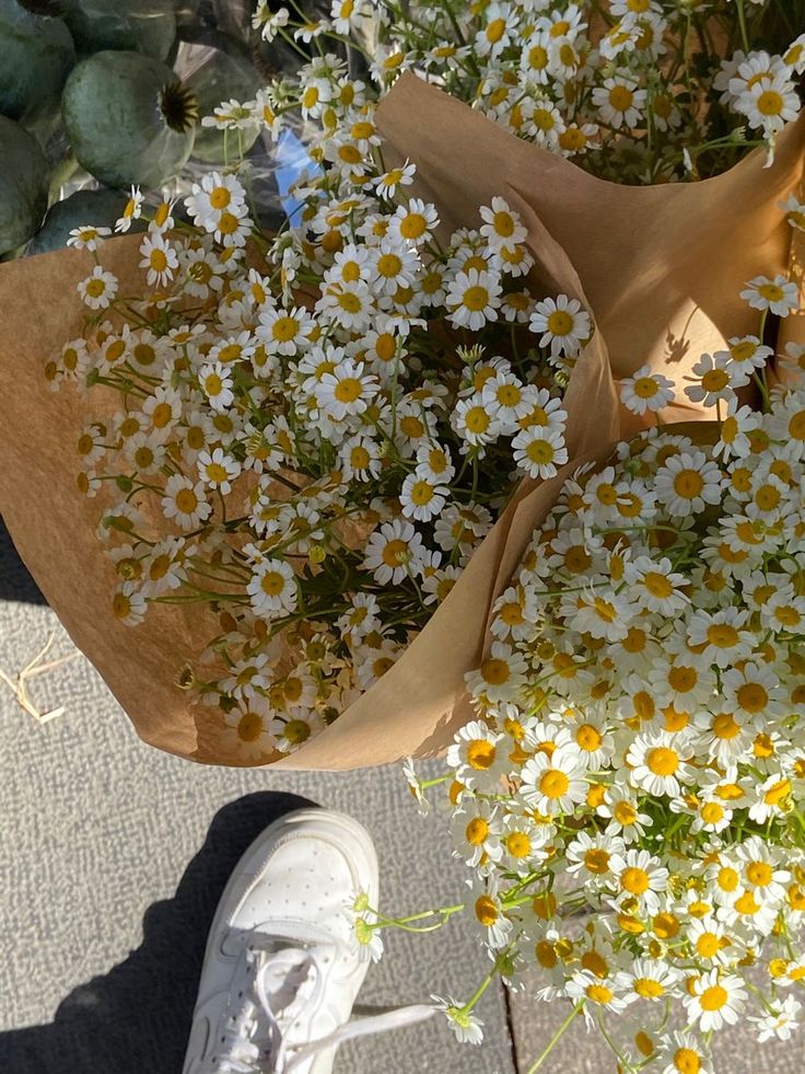 a bunch of daisies and other flowers on the ground next to someone's feet