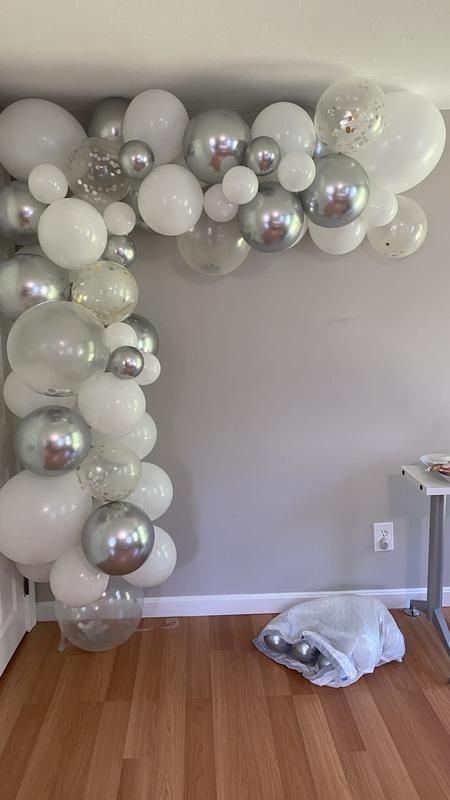 white balloons are hanging from the ceiling in front of a wall with silver and white decorations