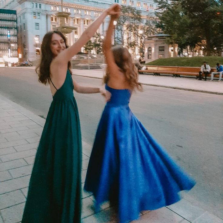 two women in long dresses dancing on the sidewalk