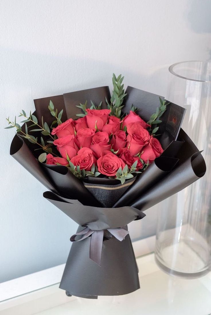 a bouquet of red roses is wrapped in black paper and placed on a white table