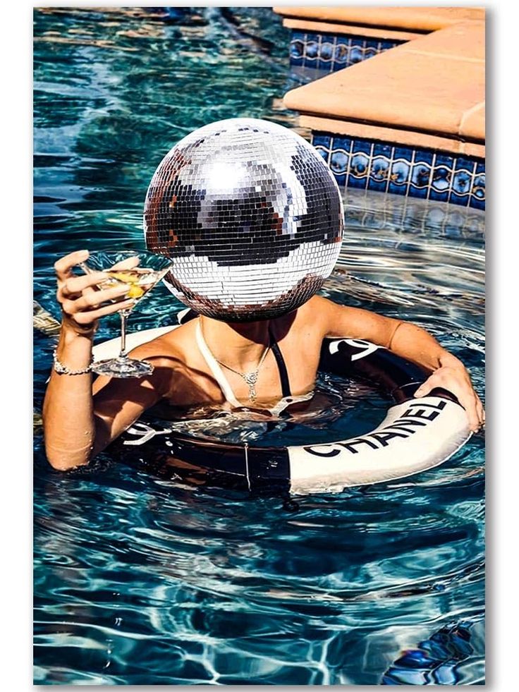 a woman in a pool with a disco ball on her head and holding a drink