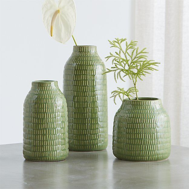 three green vases sitting on top of a table next to a white flower in a vase
