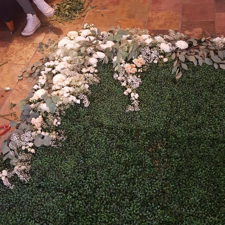 white flowers and greenery on the ground in front of a person sitting at a table