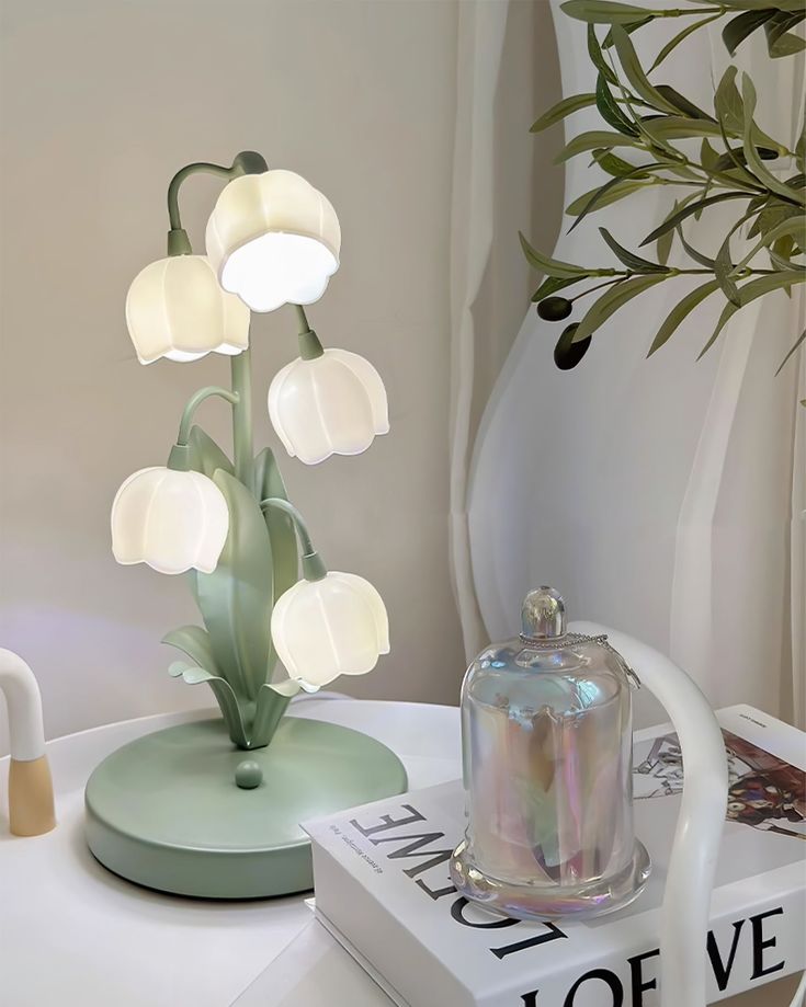 a white flower lamp sitting on top of a book next to a vase with flowers