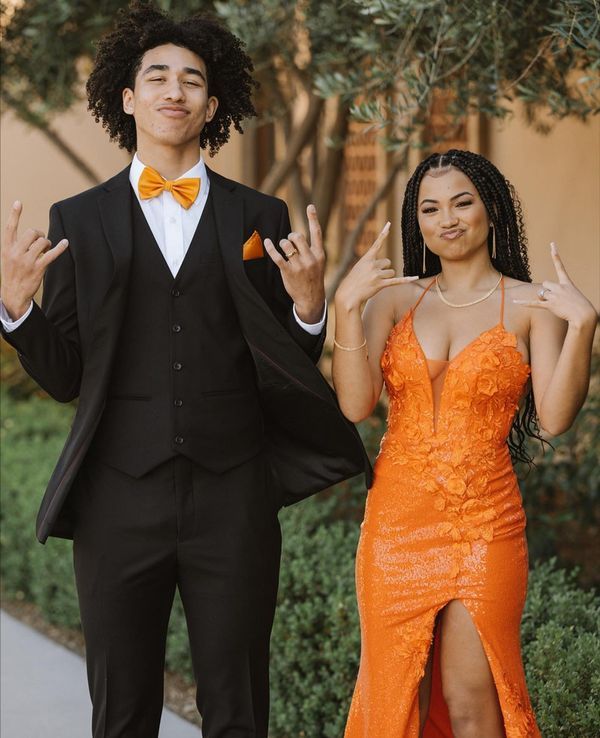 a man in a tuxedo standing next to a woman wearing an orange dress