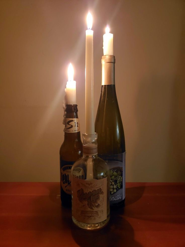 two bottles with candles in them sitting on a table next to one another and an empty bottle