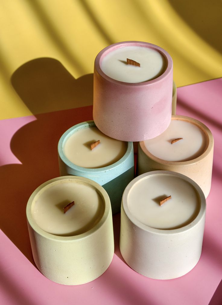 four candles sitting on top of each other in front of a yellow and pink background