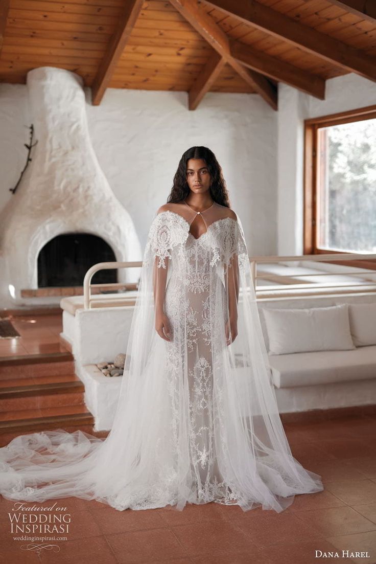 a woman in a white wedding dress standing in front of a fireplace wearing a long veil