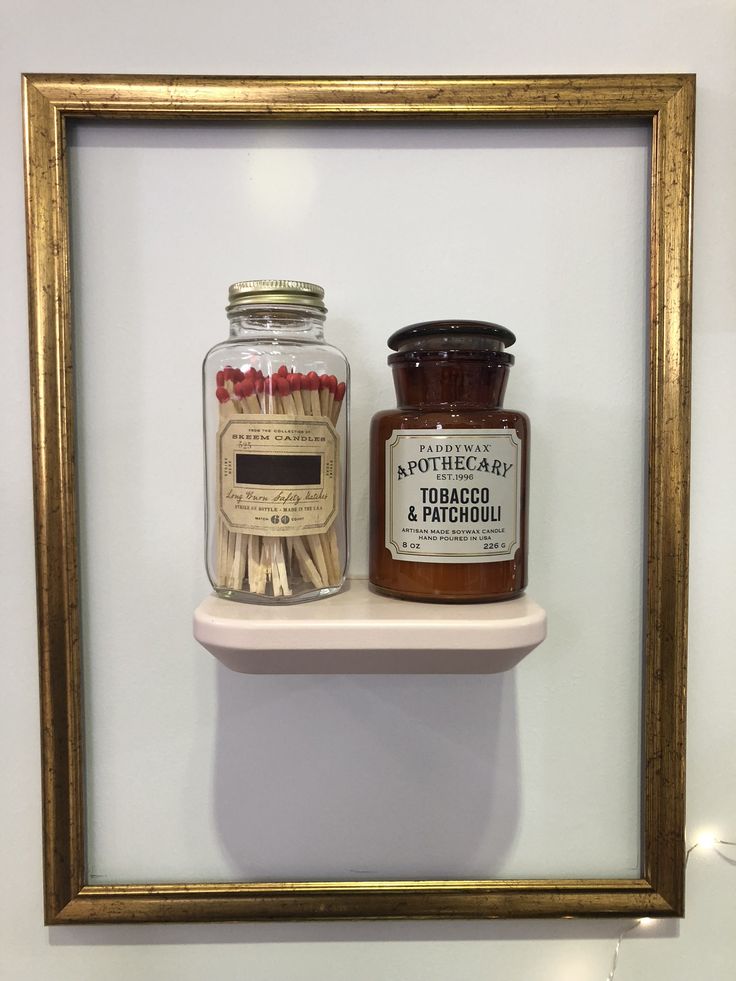 two matches are sitting on a shelf next to a jar of matches in a gold frame