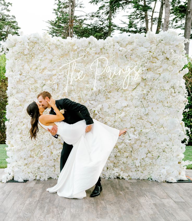 a bride and groom kissing in front of a floral backdrop