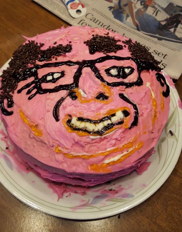 there is a pink cake with black icing on it and a face drawn on the top