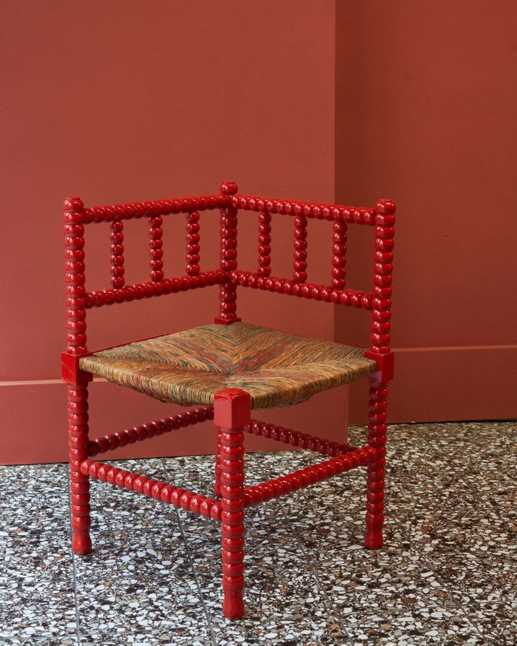 a red chair sitting on top of a floor next to a wall with beads all over it