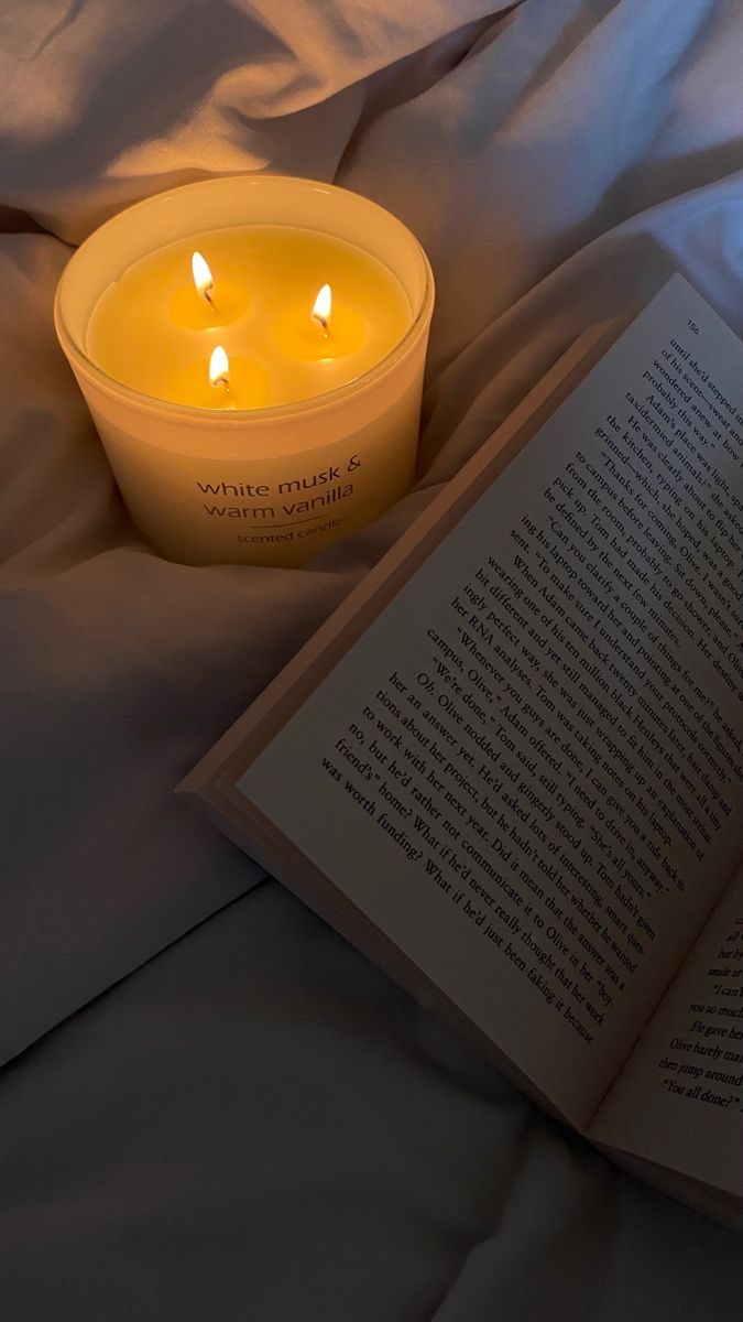 an open book sitting on top of a bed next to a lit candle