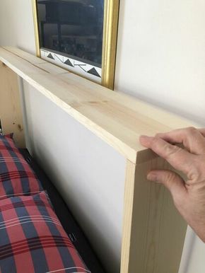 a person is holding the edge of a wooden shelf above a bed with a red and black checkered pillow