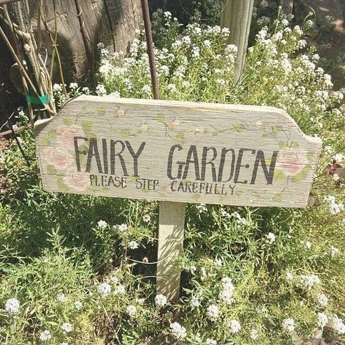 a wooden sign that says fairy garden in front of some bushes and flowers on the ground