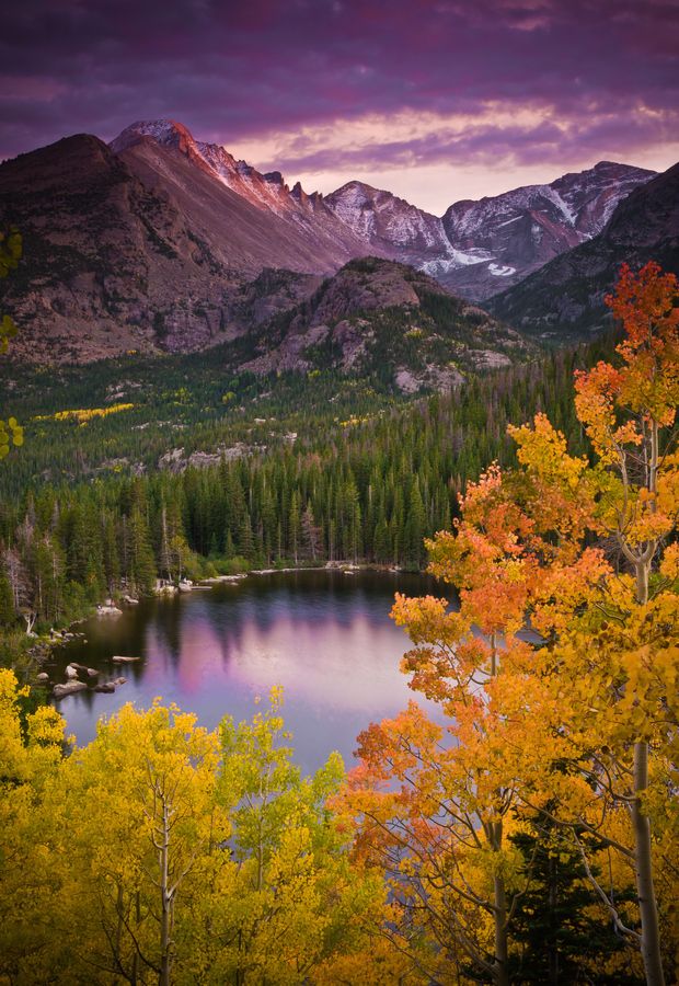 a lake surrounded by trees with mountains in the background and clouds above it at sunset
