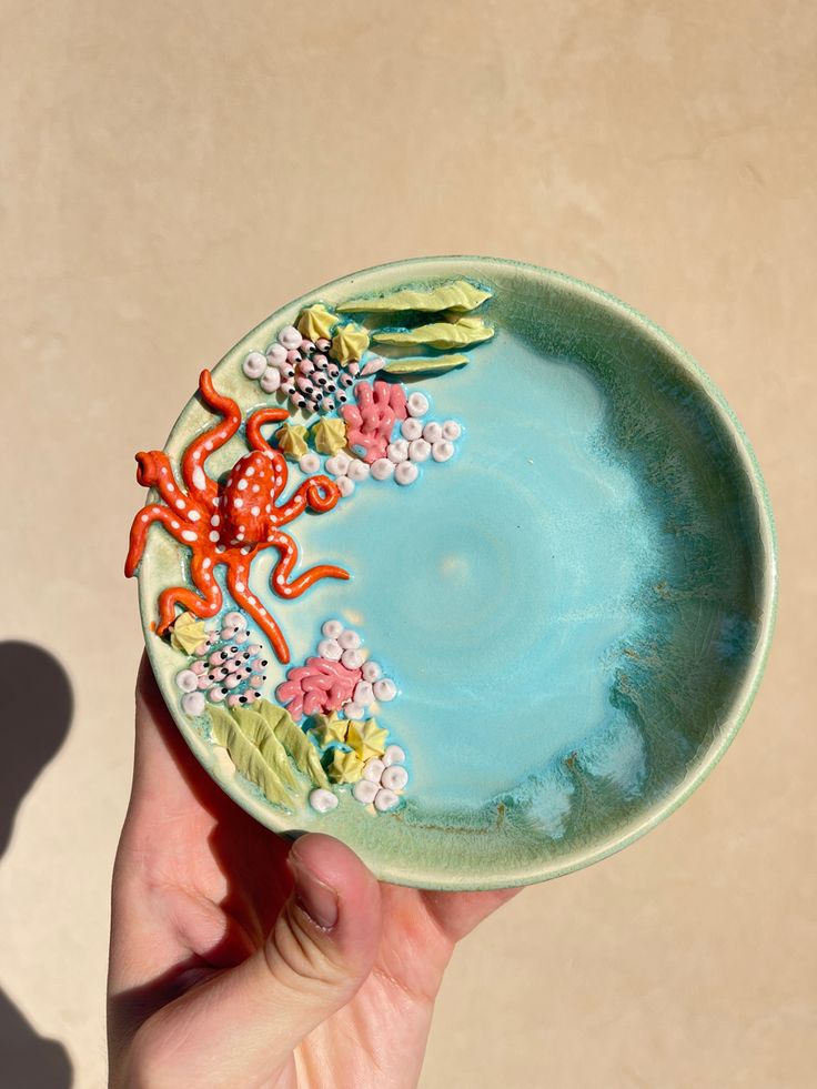 a hand holding a decorative plate with an octopus on the front and corals on the back