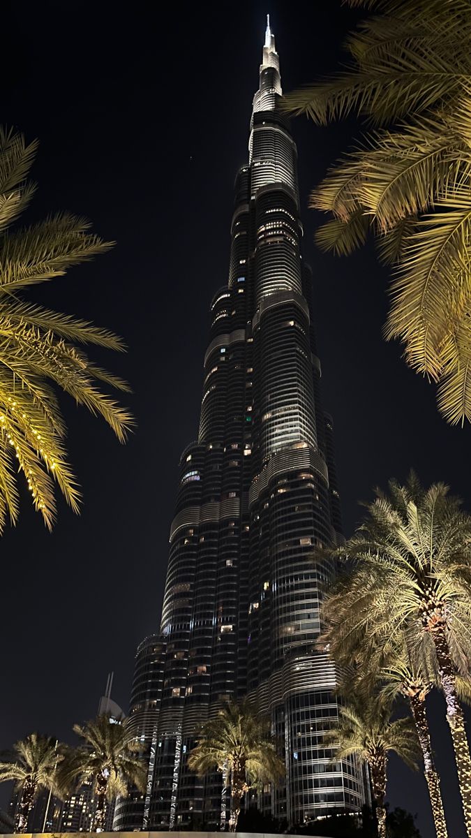 the burj tower is lit up at night with palm trees in front of it