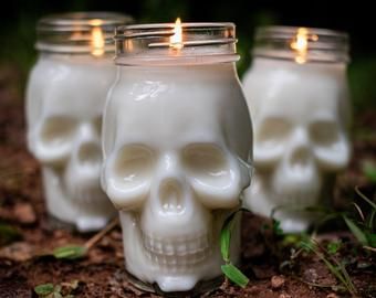 three white candles with skulls on them sitting in the dirt