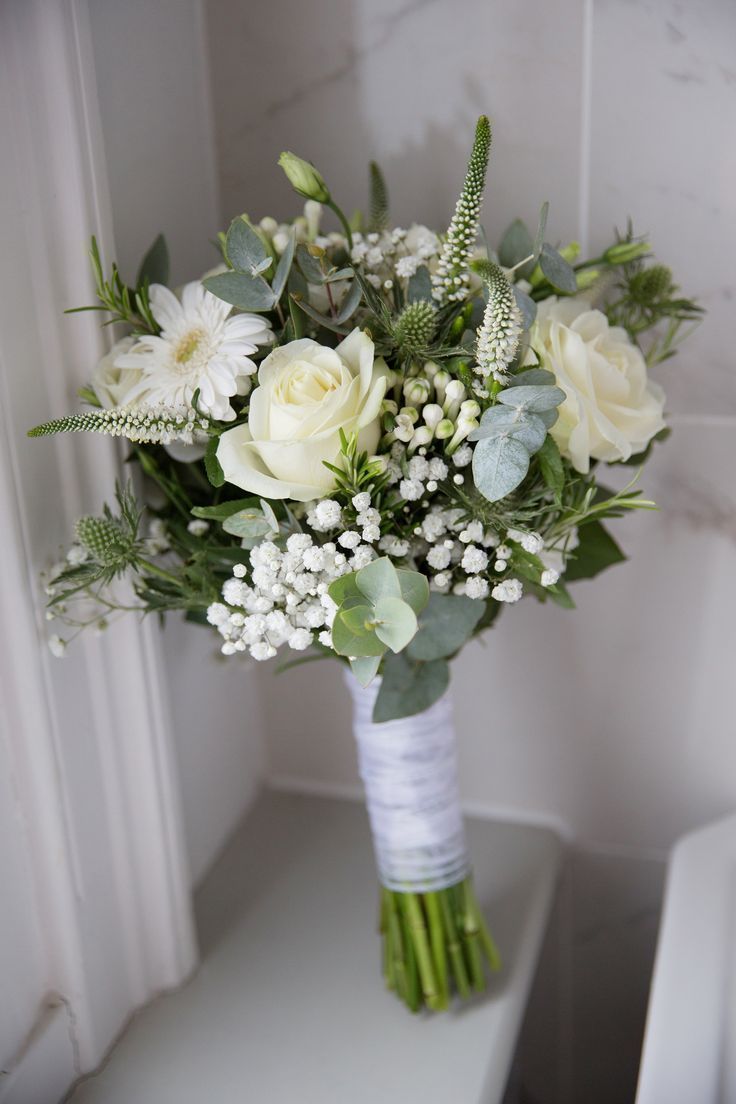 a bouquet of white flowers and greenery on a shelf next to a window sill