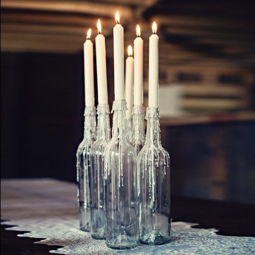 there are many candles that are in the glass bottles on the tablecloth with white lace