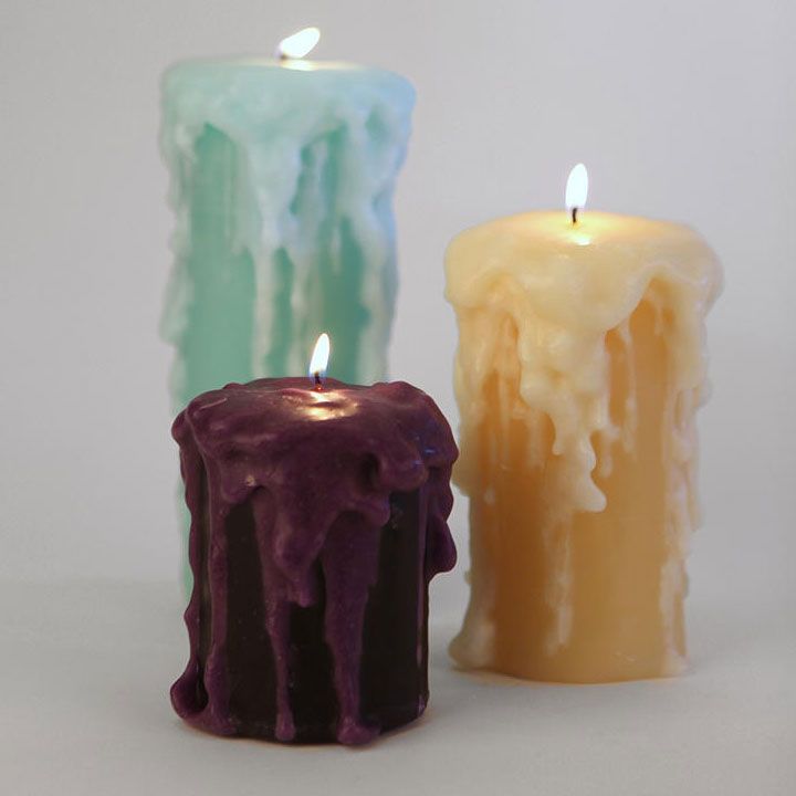 three different colored candles sitting next to each other on a white surface with one candle lit