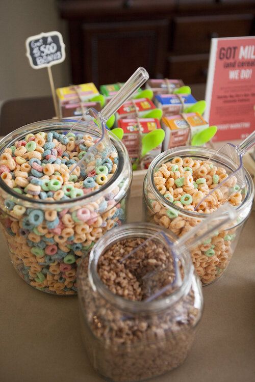 three glass jars filled with cereal on top of a table next to candy bar signs