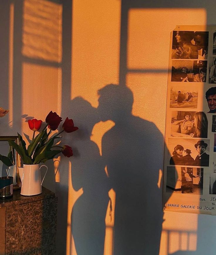 the shadow of a man standing next to a vase with flowers