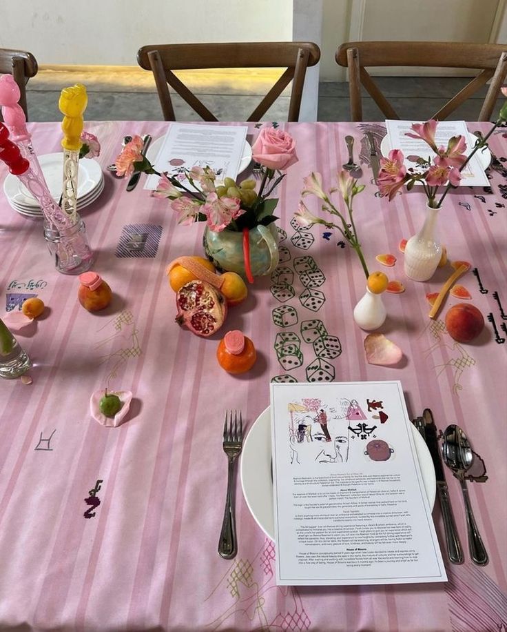 the table is set with pink and white striped cloths, silverware, flowers, and fruit