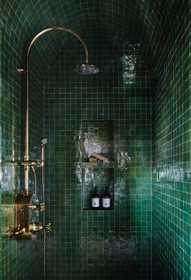 a green tiled bathroom with gold faucet and shower head